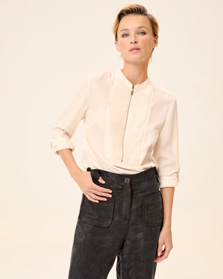 Mujer con blusa beige elegante, combinada con pantalón negro y tacones.