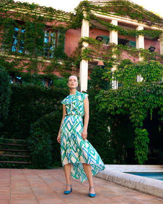 Mujer con blusa con lazo, posando en un entorno con vegetación y arquitectura.