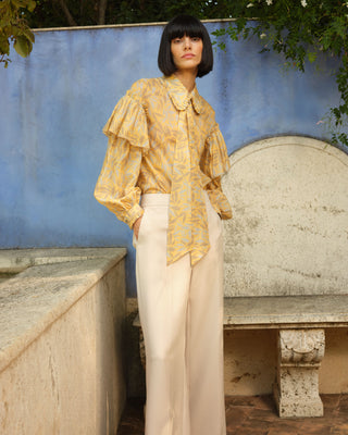 Mujer con blusa flores, posando en un entorno con arquitectura clásica y vegetación.