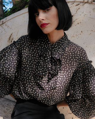 Mujer con blusa lunares, posando con falda corta y tacones elegantes.