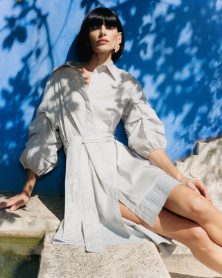 Mujer con vestido corto camisero, sentada sobre una roca con luz natural.