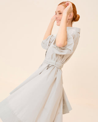 Mujer con vestido corto camisero, girando con los brazos en alto y expresión alegre.