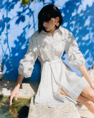 Mujer con vestido corto camisero, combinando con zapatos planos en un entorno natural.